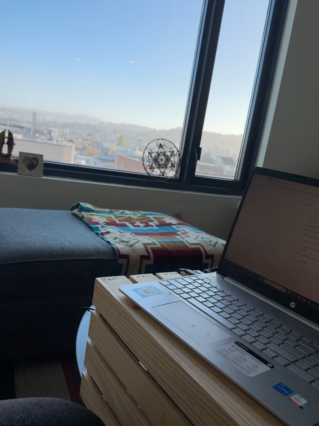 AstroTAROT development workspace on the ninth floor overlooking San Francisco, with a laptop and sacred geometry on the windowsill.